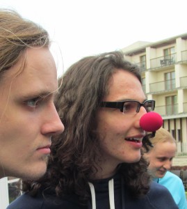 Drei Personen, Blick nach rechts, in der Mitte mit roter Clowns-Nase