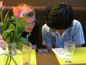 Zwei Contestants beugen sich über ein Mobiltelefon, der vorherige Blog-Eintrag geöffnet.